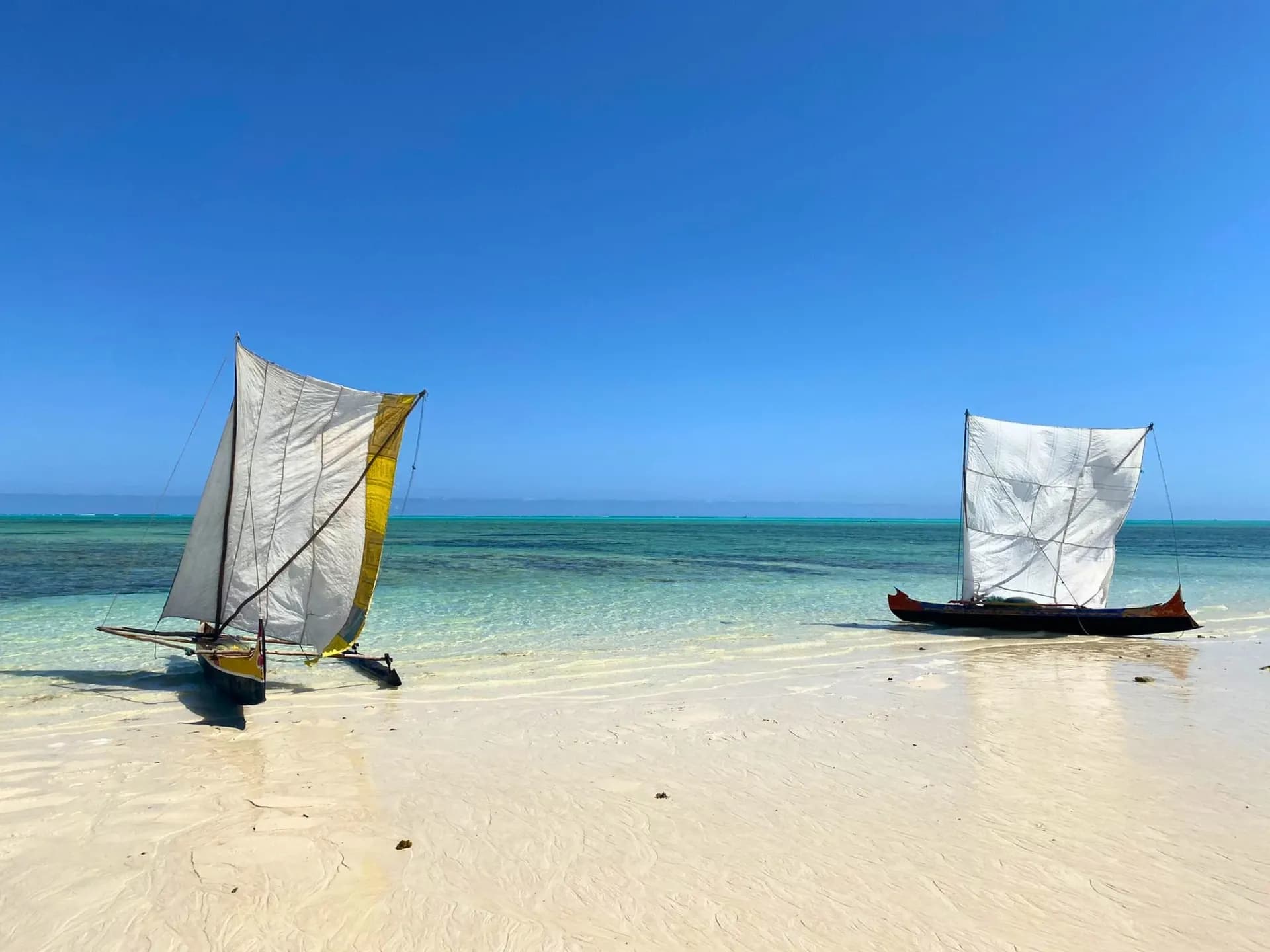 Deux voiliers traditionnels sur une plage de sable blanc aux eaux turquoise cristallines sous un ciel dégagé