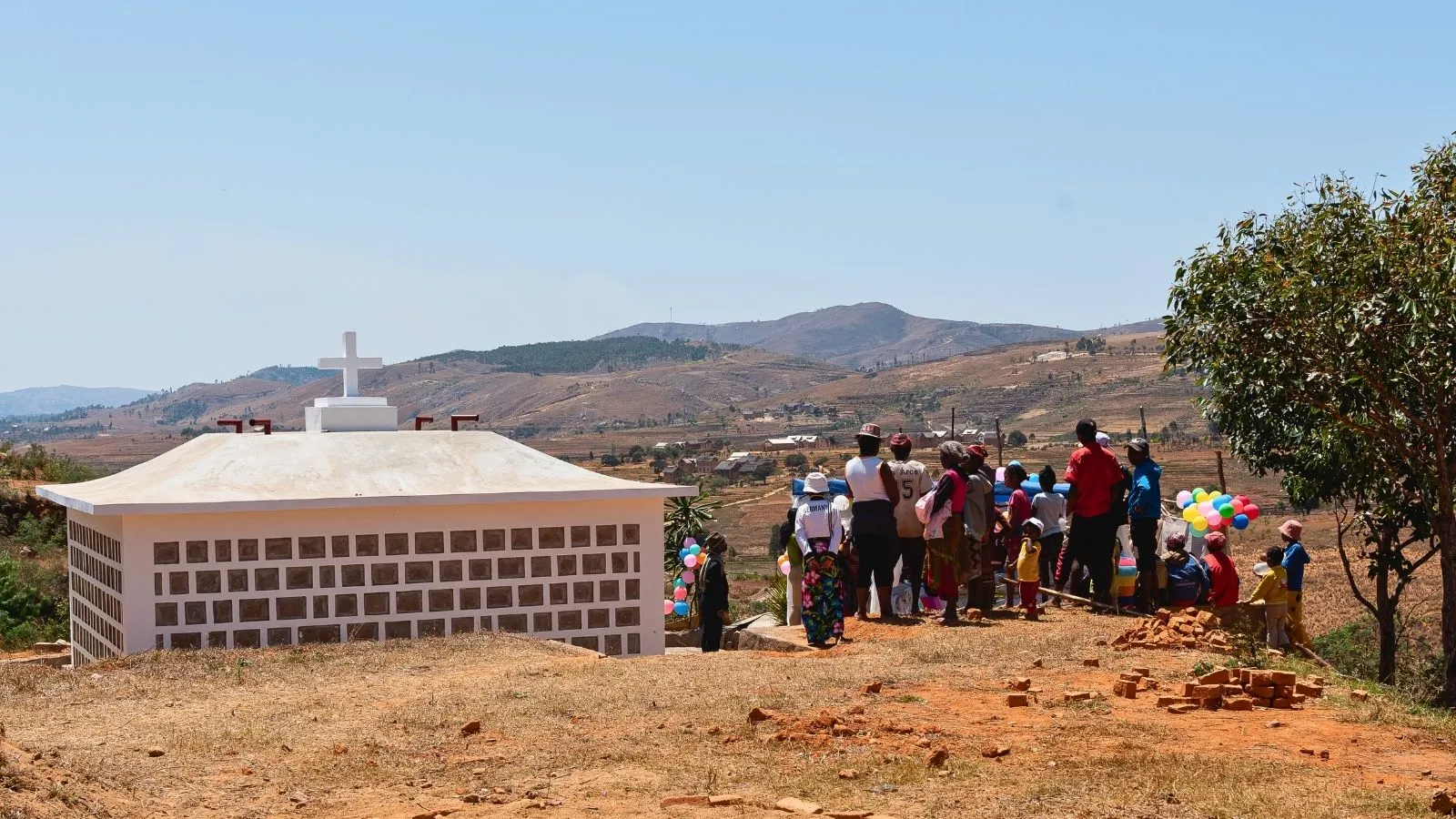 Assemblée festive devant une petite église en construction dans un paysage rural malgache sous ciel dégagé