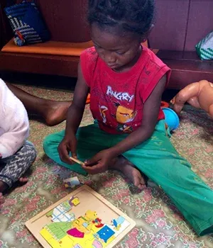 Enfant à Madagascar assemblant une puzzle éducatif coloré avec un maillot rugby