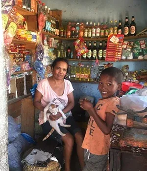 Deux personnes souriantes dans une petite épicerie malgache remplie de produits locaux variés