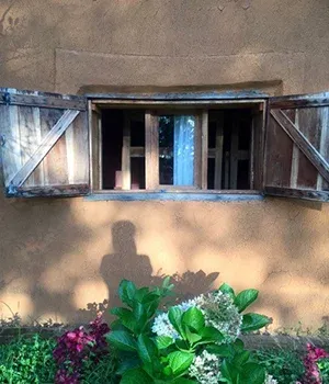 Maison en terre avec fenêtres ouvertes et fleurs colorées projetant une ombre sur le mur