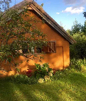 Maison en torchis colorée orange entourée de végétation luxuriante sous un ciel dégagé