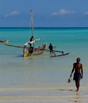 Un homme marche sur une plage de sable blanc près d’un voilier traditionnel à Madagascar