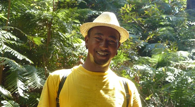 Voyageur souriant en chapeau de paille jaune dans un environnement tropical verdoyant à Madagascar