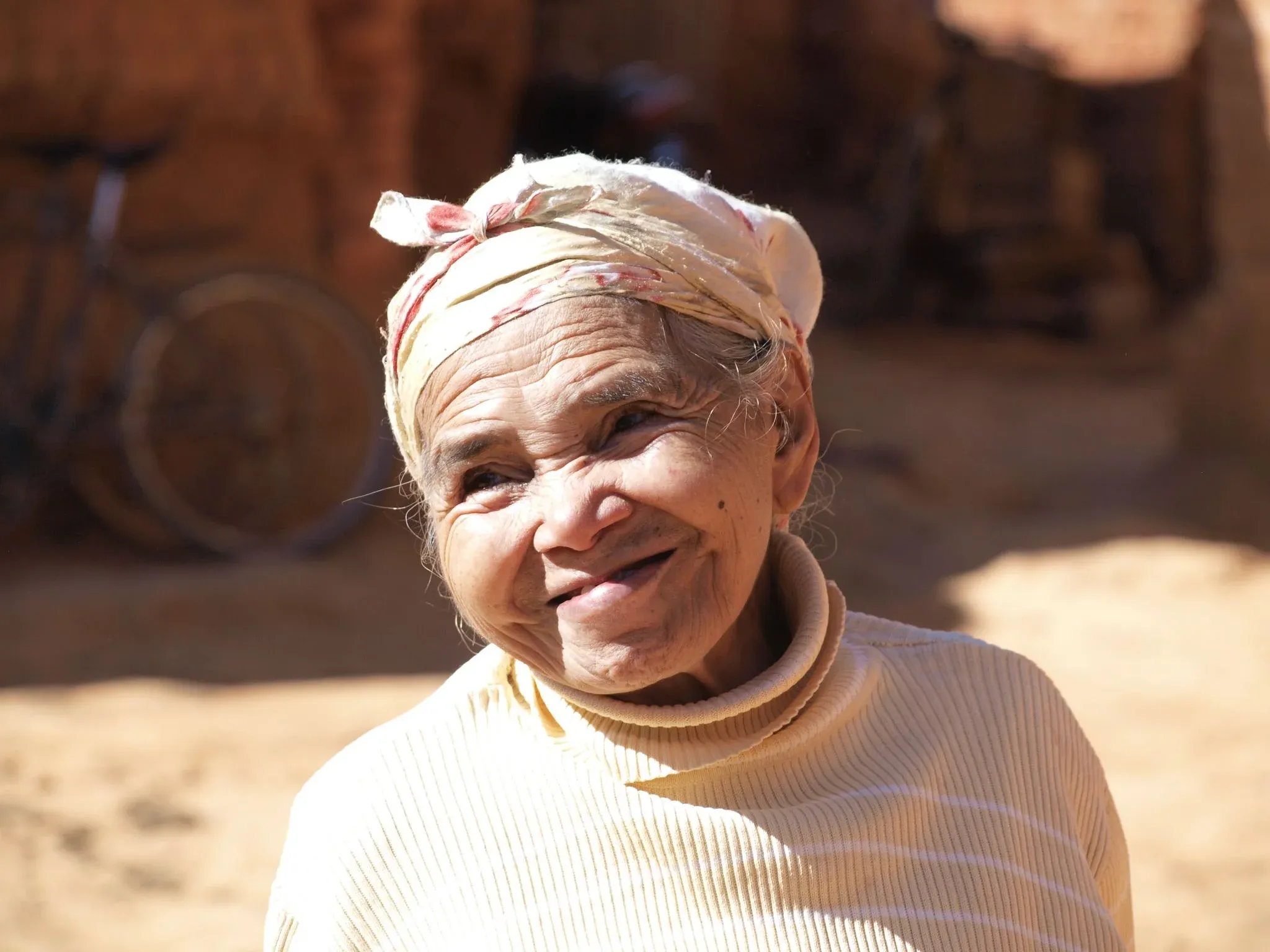 Souriante femme âgée en tenue traditionnelle devant un paysage rural malgache