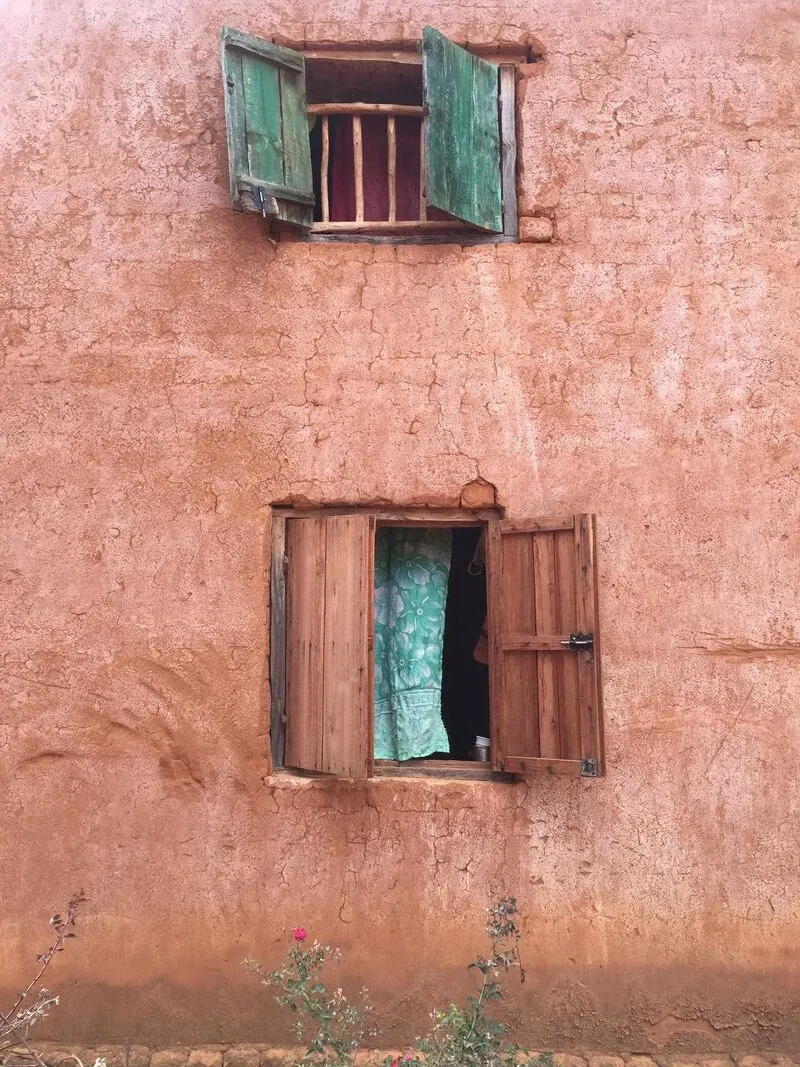 Maison en terre rouge avec fenêtre en bois ouverte et rideau coloré à Madagascar