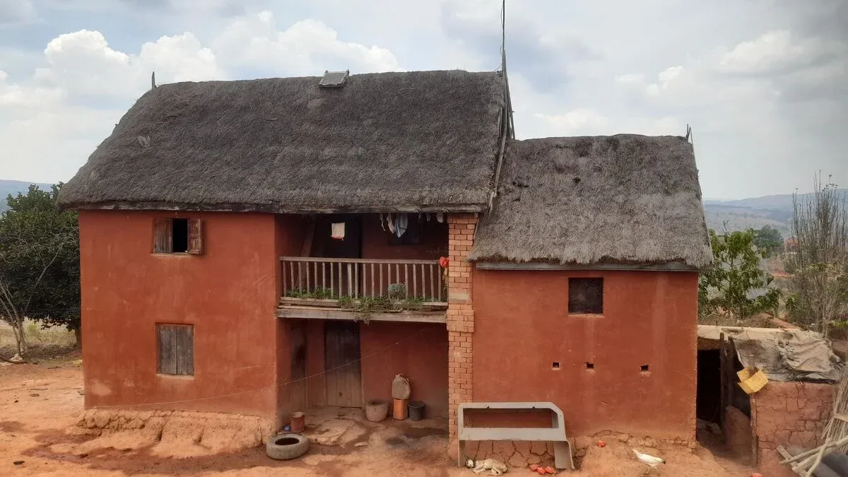 Maison traditionnelle en terre et toiture de chaume avec balcon en région rurale malgache