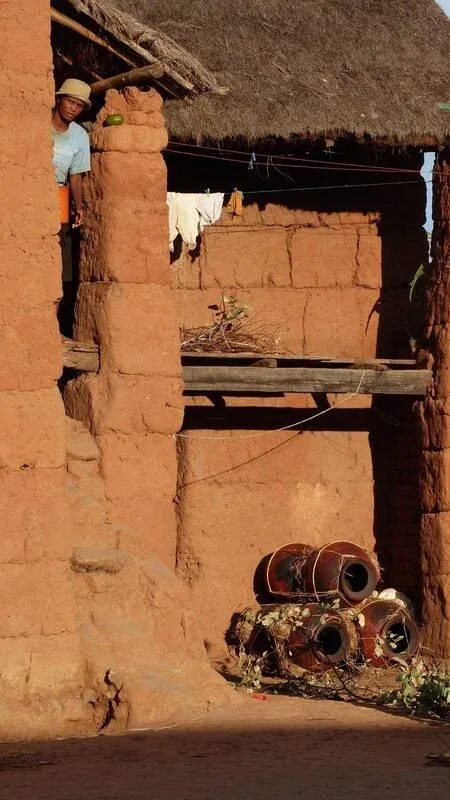 Habitant penché observant depuis une fenêtre en terre d’une maison traditionnelle avec poteries en bas