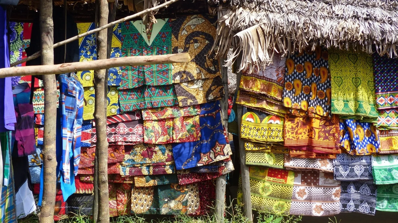 Étagères colorées de tissus traditionnels malgaches exposés sous abri en paille et bois à Madagascar