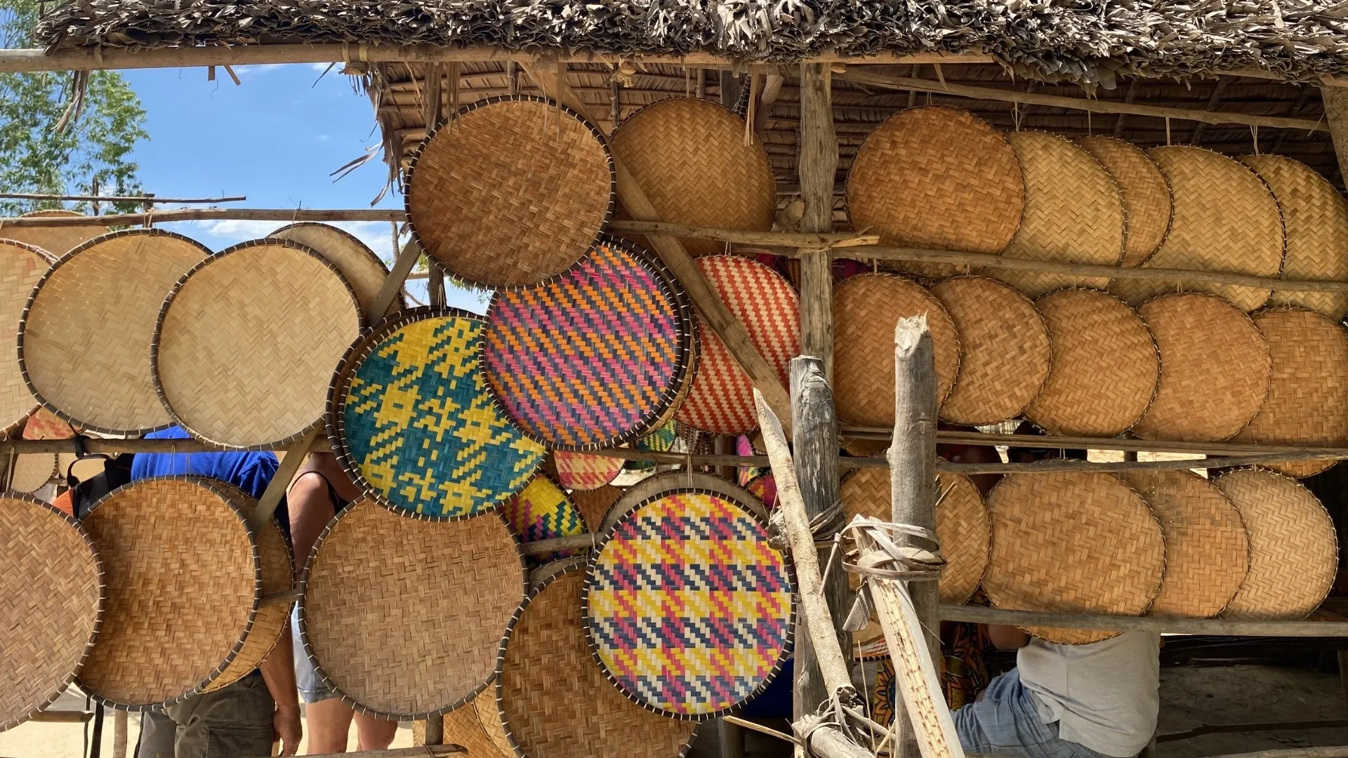 Paniers en rotin et plats tissés colorés exposés sous abri en paille à Madagascar