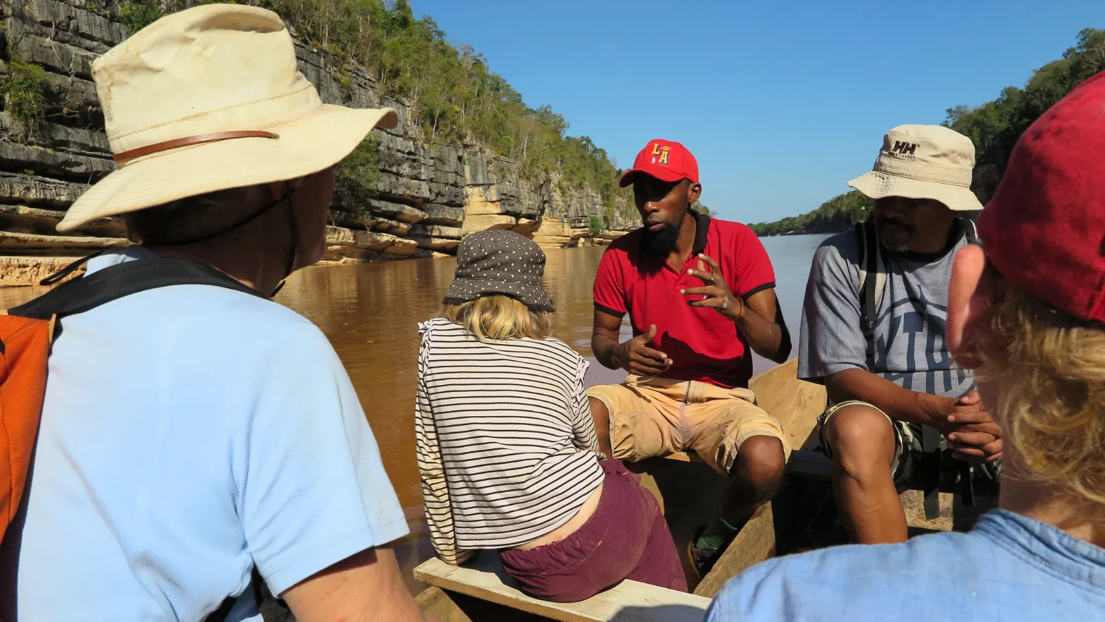 Groupe en excursion sur une pirogue discutant avec un guide près de falaises rocheuses en bord de rivière