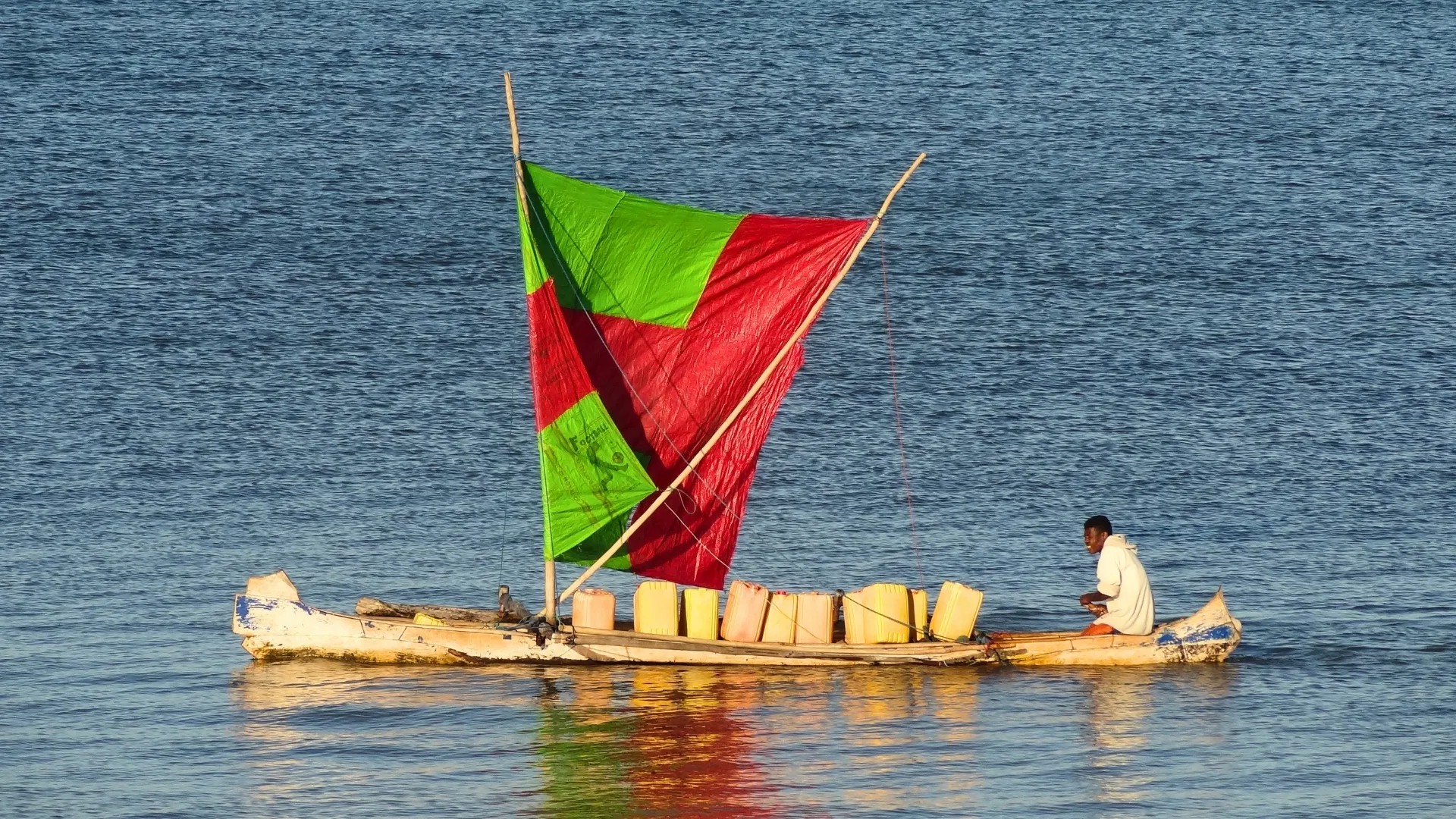 Pirogue traditionnelle malgache avec voile rouge et verte chargée de sacs sur l’eau