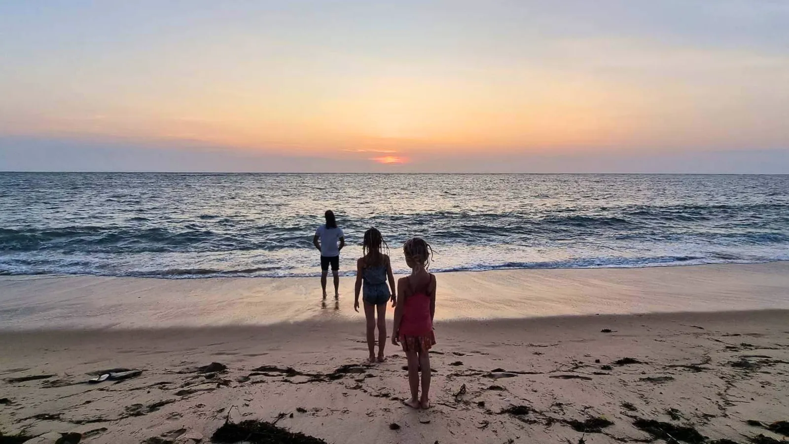 Une famille marche sur une plage au coucher de soleil face à l'océan