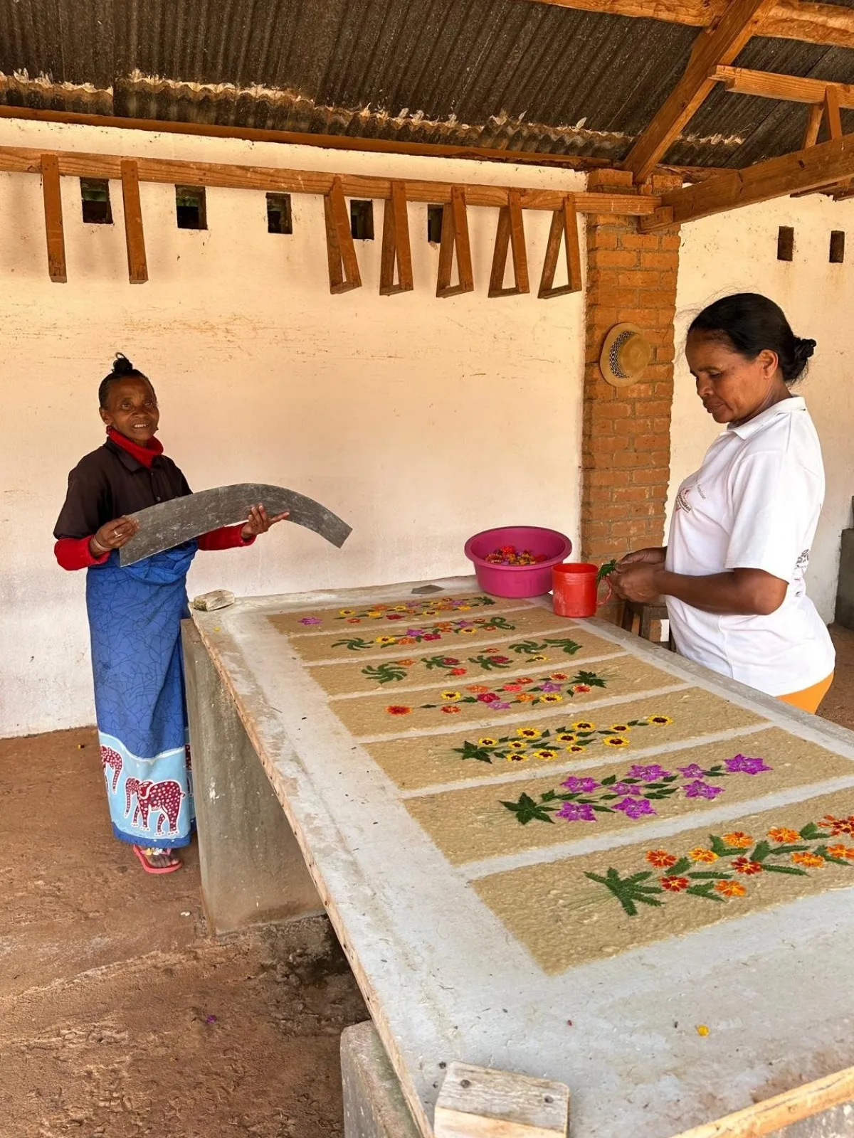 Deux artisanes à Madagascar réalisant des batiks traditionnels colorés sur des tissus étendus