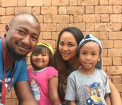 Famille souriante devant un mur en briques avec deux enfants et deux adultes en tenue décontractée