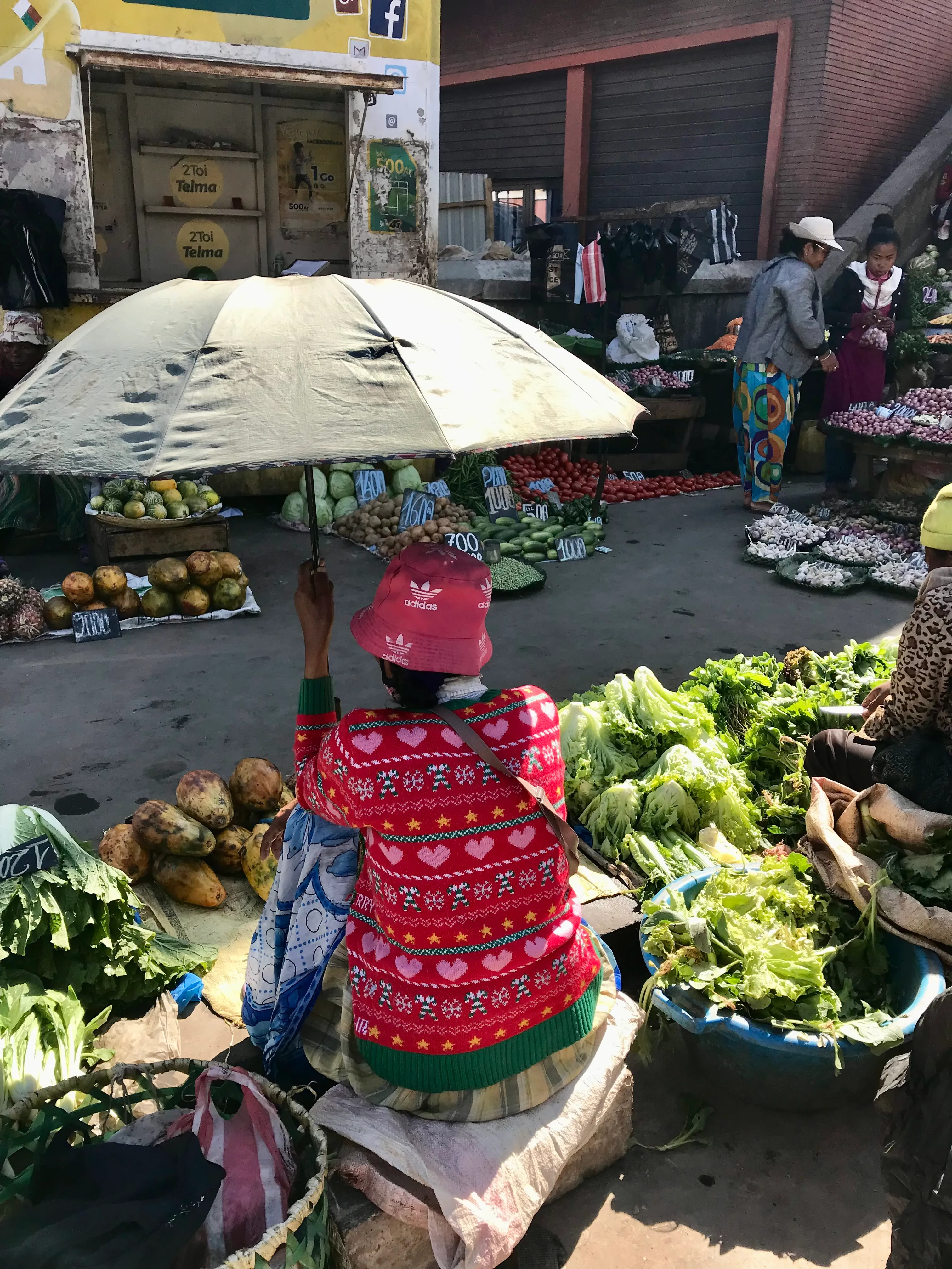 Marché malgache femme sous parapluie vendant légumes et fruits colorés