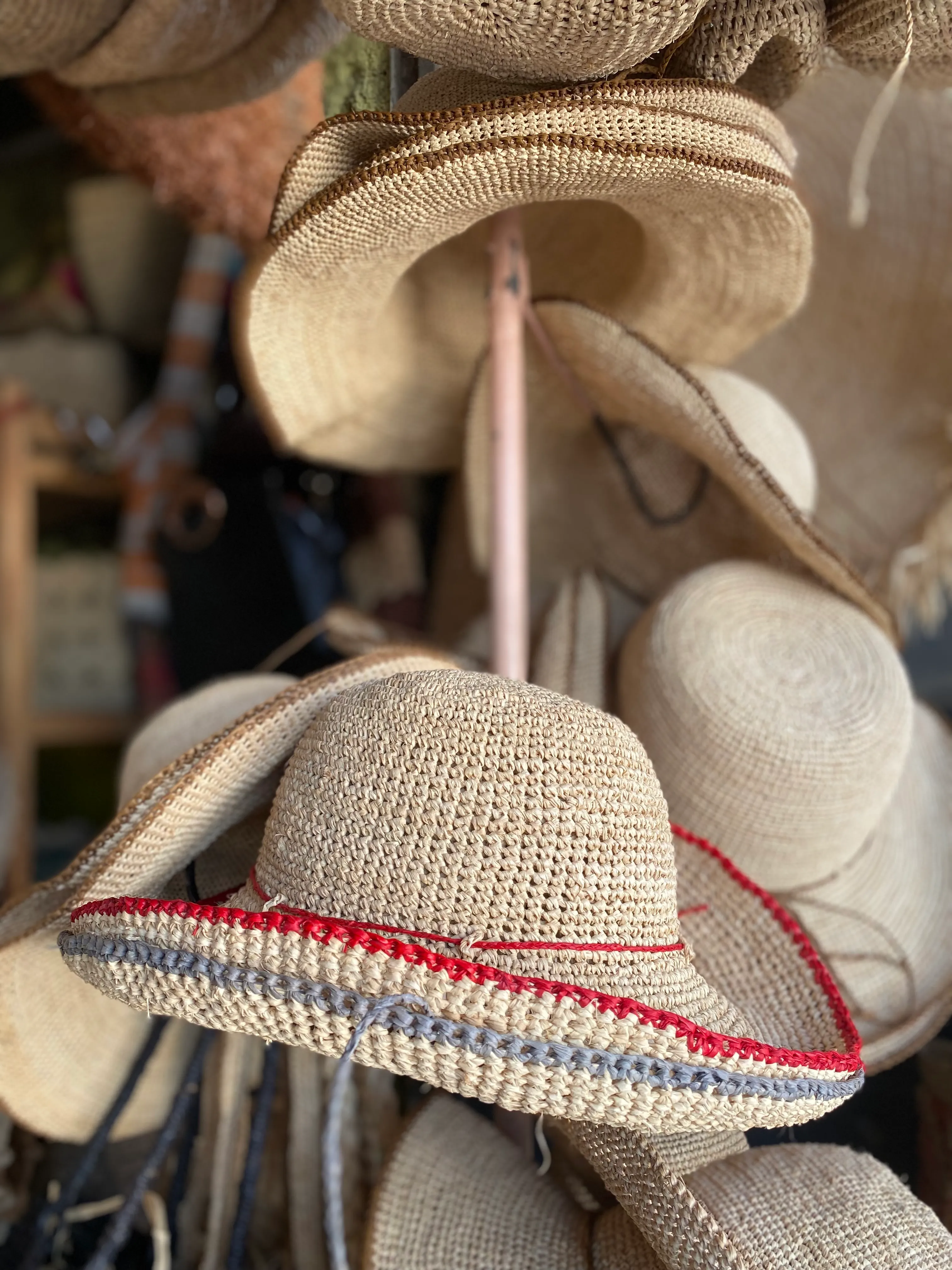 Chapeau en jute tressé coloré rouge et bleu suspendu parmi d'autres modèles artisanaux