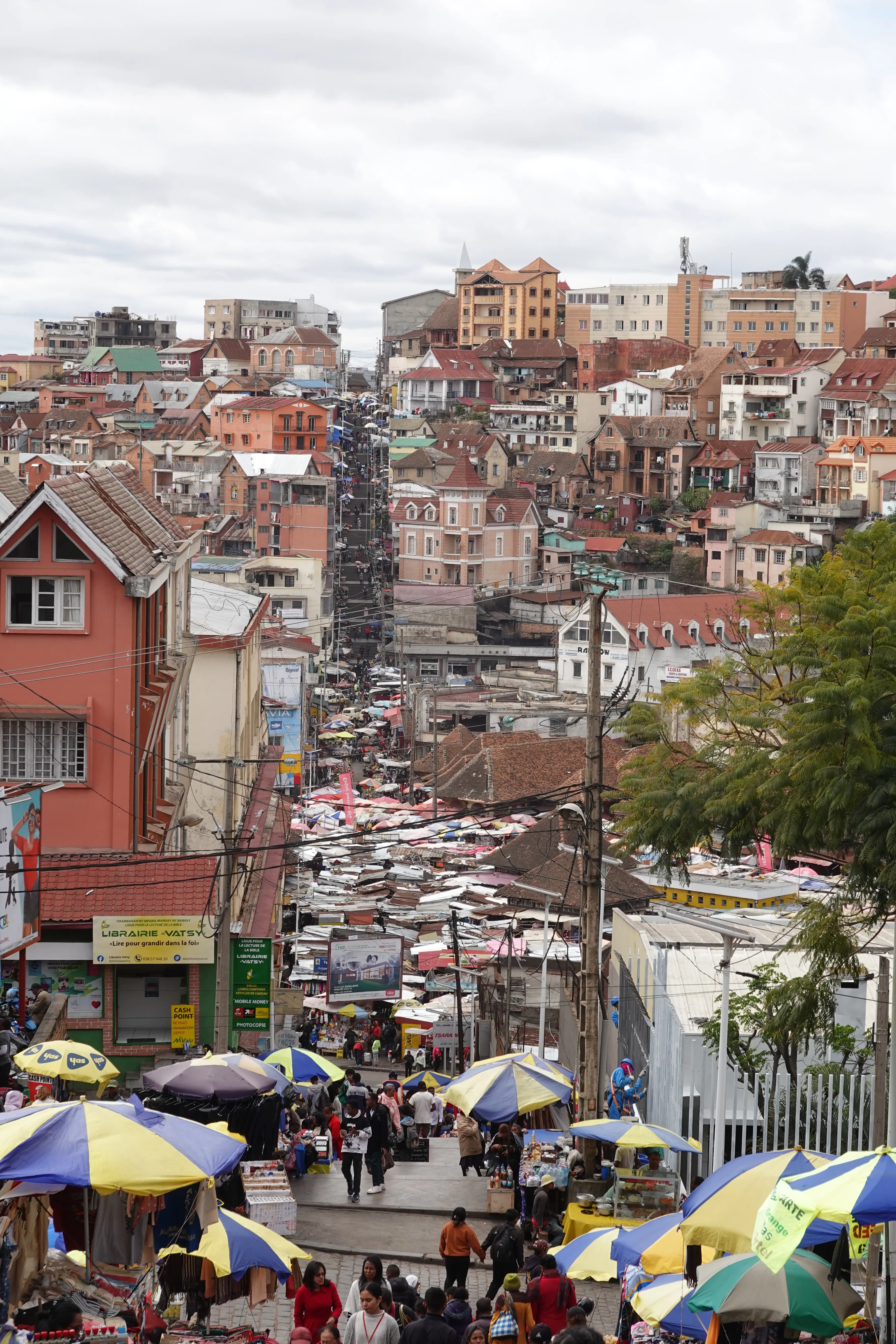 Marché animé en pente dans une ville malgache aux toits colorés et étals sous parasols