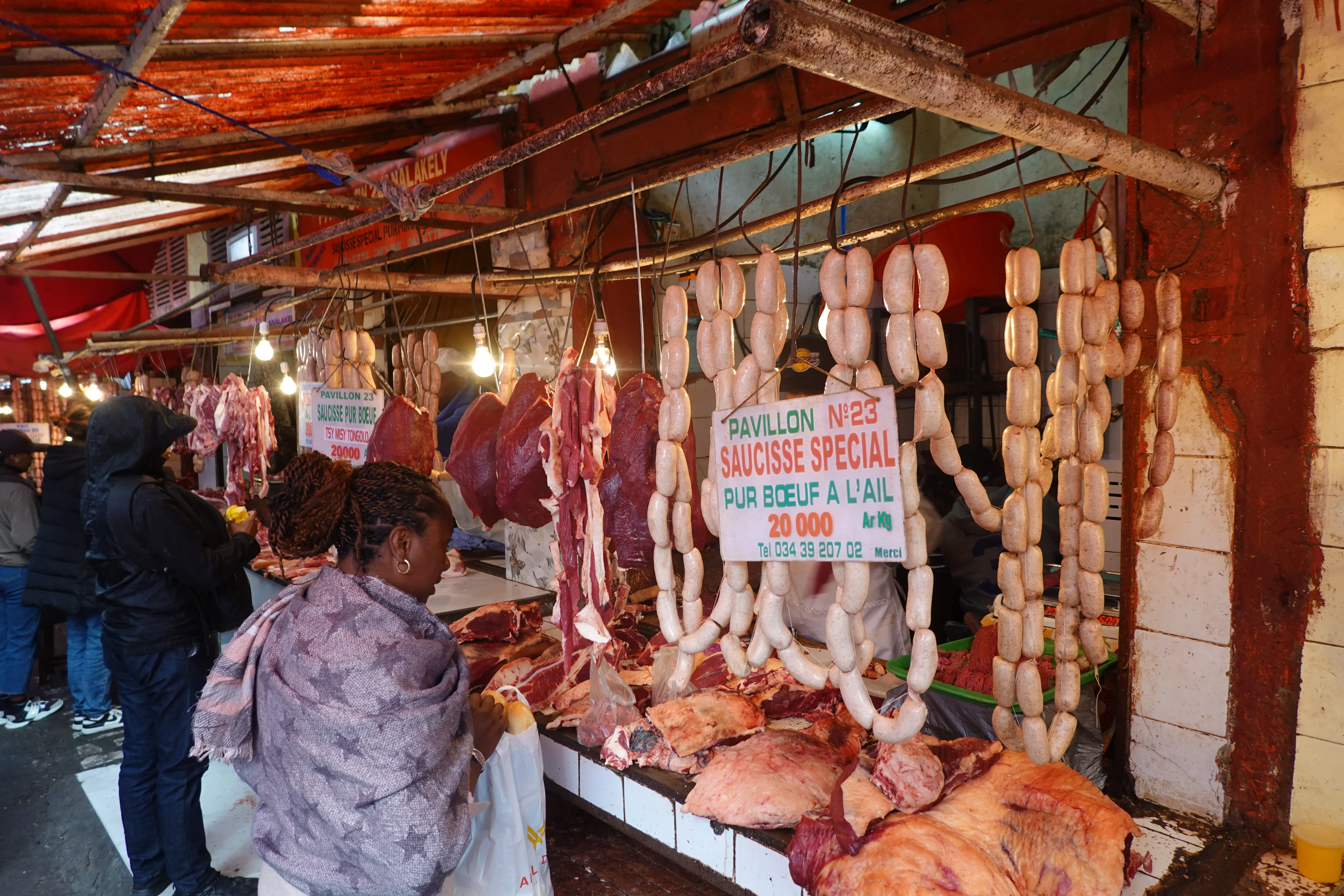 Marché malgache étal de charcuterie et viandes séchées avec clients intéressés