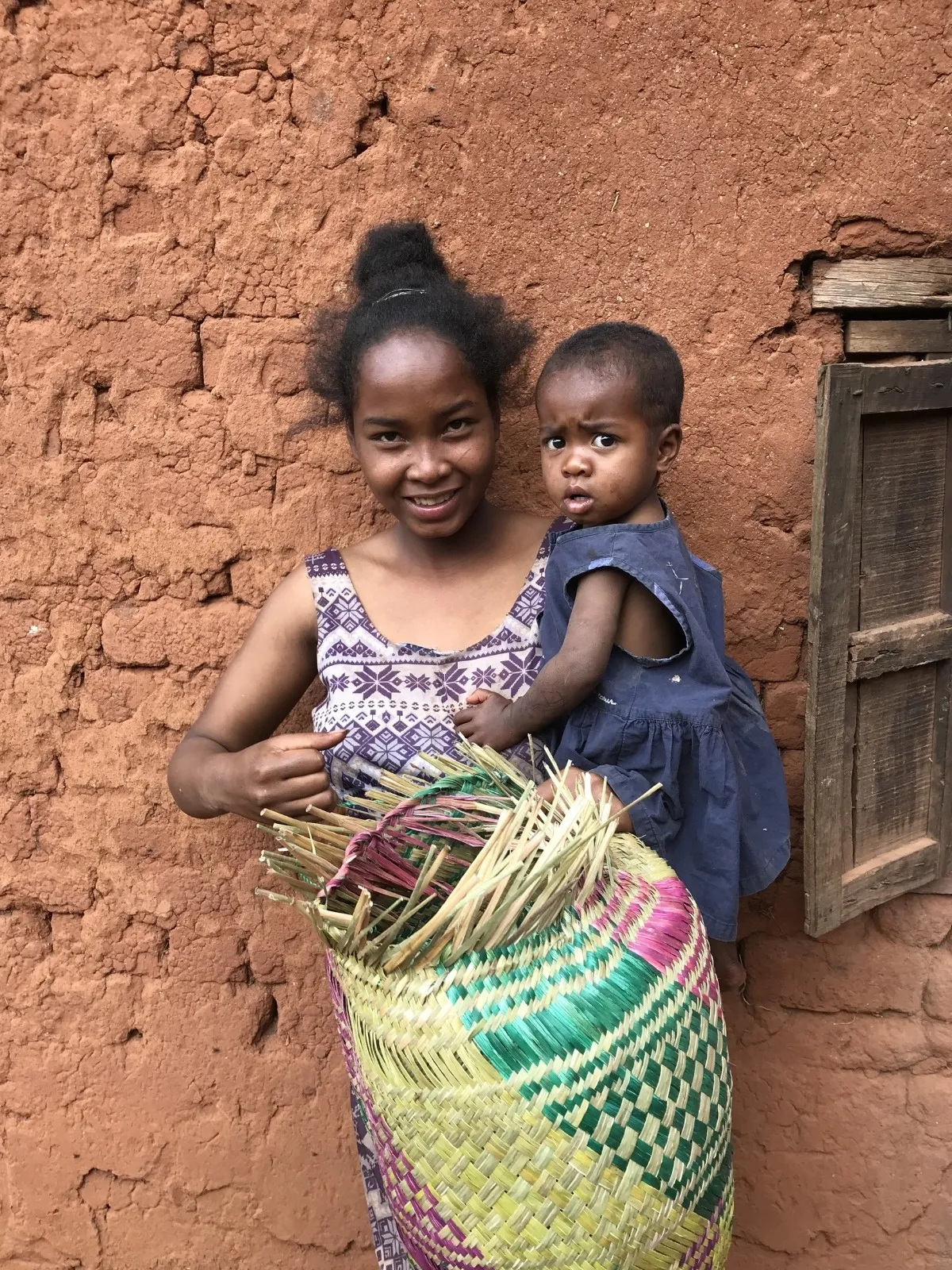 Deux petites filles devant une maison en terre avec un panier artisanal coloré