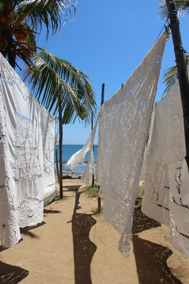 Broderies séchant sous palmiers face à une plage et l’océan bleu de Madagascar