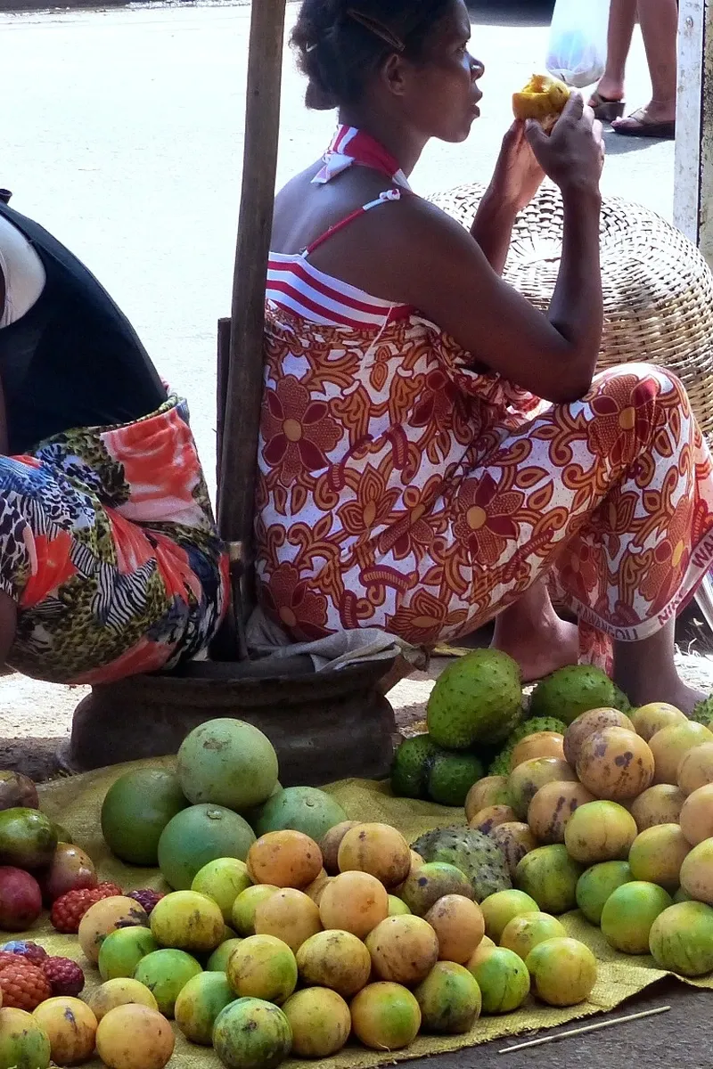 Marchande malgache dégustant des fruits exotiques devant son étalage coloré