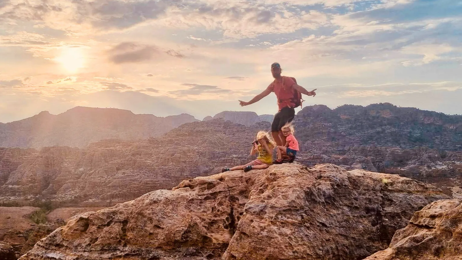 Randonneurs au coucher de soleil sur un rocher dominant un paysage montagneux aride