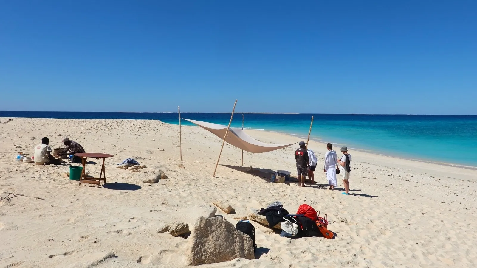 Plage de sable blanc à Madagascar avec tente suspendue et groupe de randonneurs près de l’océan turquoise