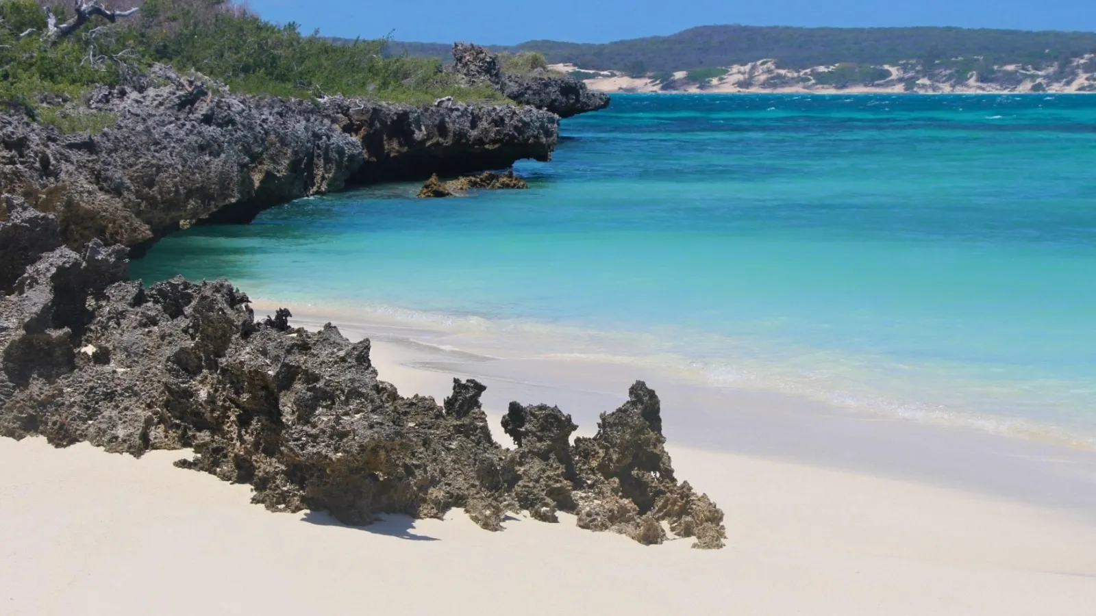 Plage de sable blanc aux eaux turquoise bordée de rochers volcaniques sous un ciel dégagé