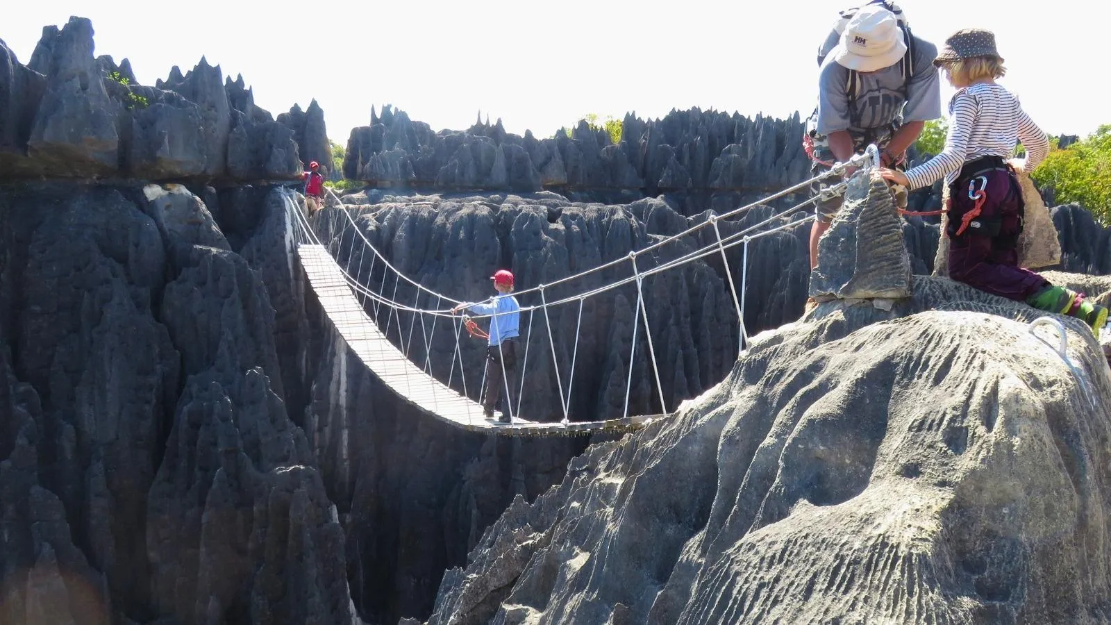 Pont suspendu spectaculaire entre falaises rocheuses avec familles en exploration à Tsingy de Bemaraha Madagascar