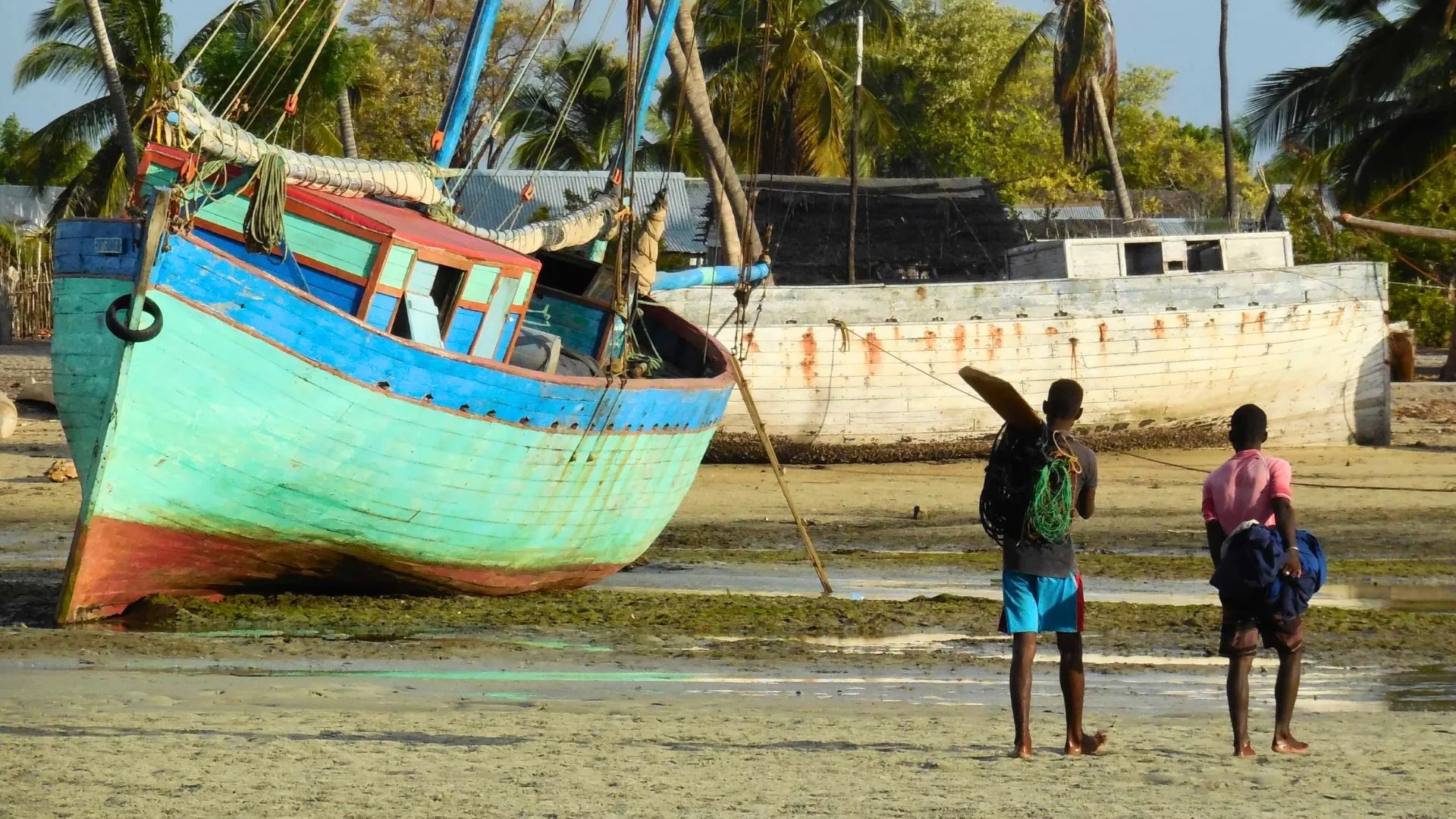 Deux hommes sur une plage de Madagascar près de bateaux de pêche colorés et vétustes sous les palmiers