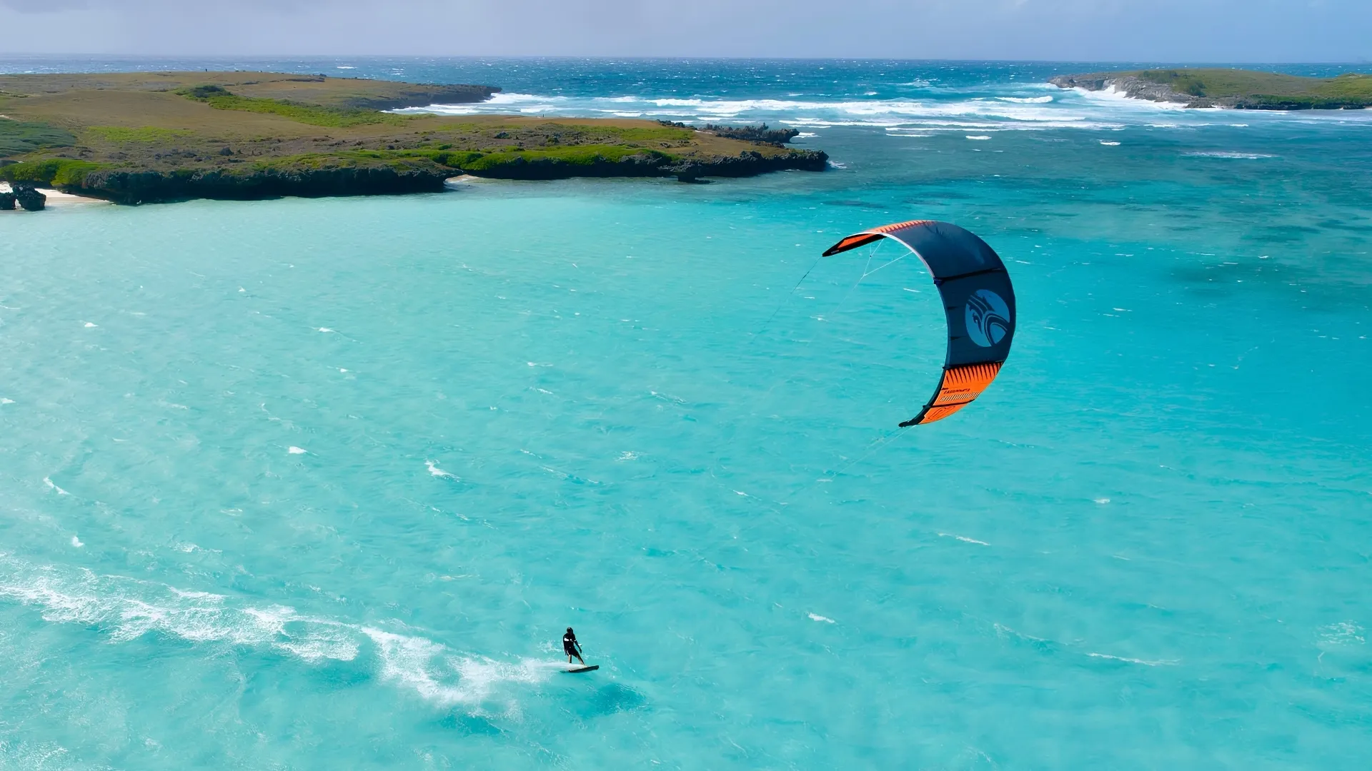 Un personne faisant du kitesurf et glissant sur des eaux turquoise près d’une côte rocheuse à Madagascar