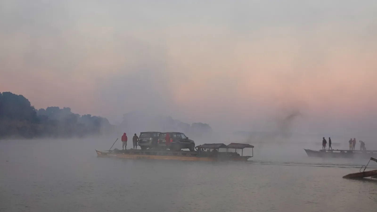 Bateau transportant un véhicule au lever du soleil dans une brume matinale sur un lac paisible à Madagascar