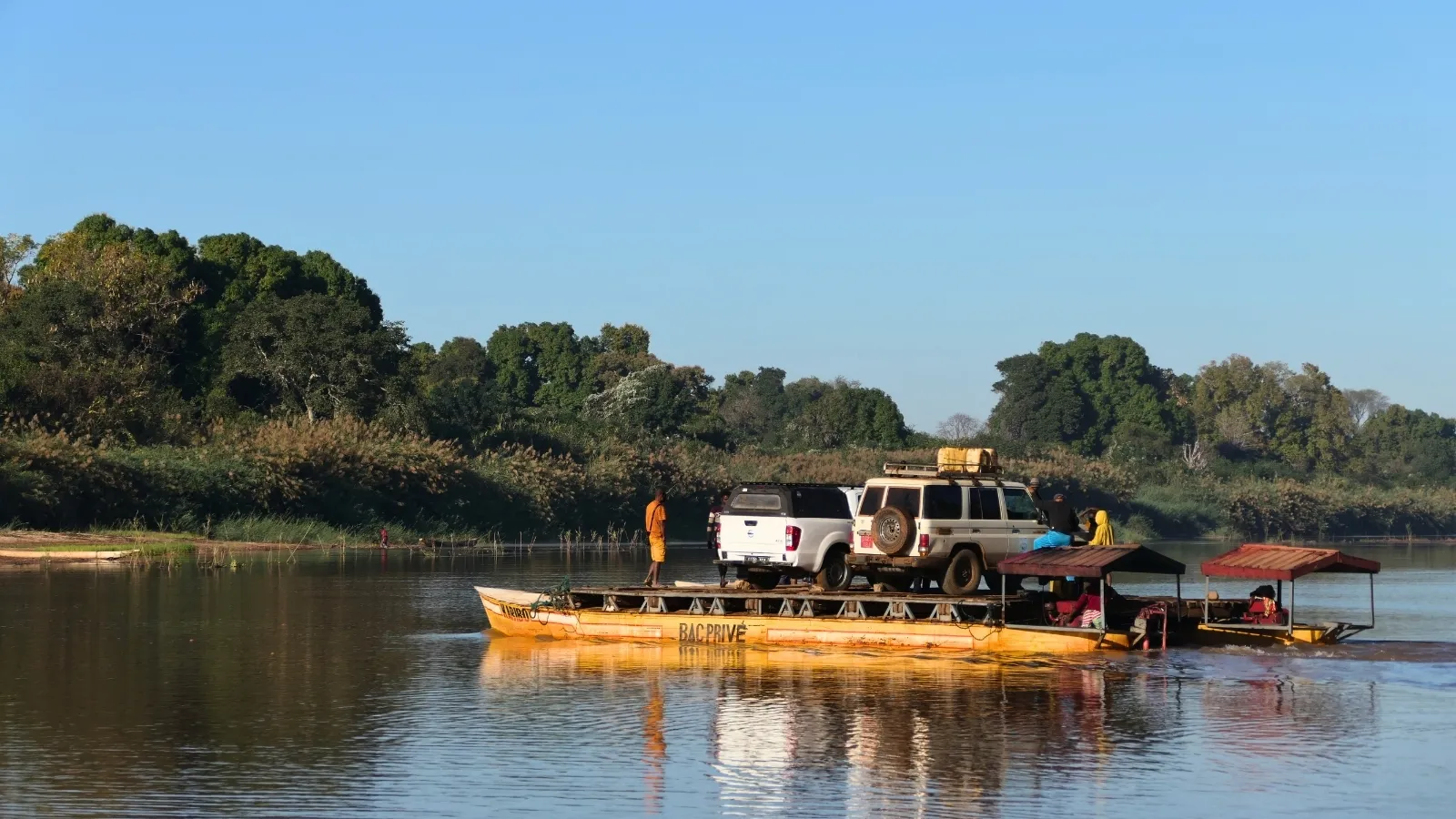 Bateau de transport de véhicules traversant une rivière entourée de végétation dense sous un ciel clair à Madagascar